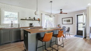 A modern kitchen with a central island, bar stools, pendant lighting, and a ceiling fan. - Hillside Haven (Faber)