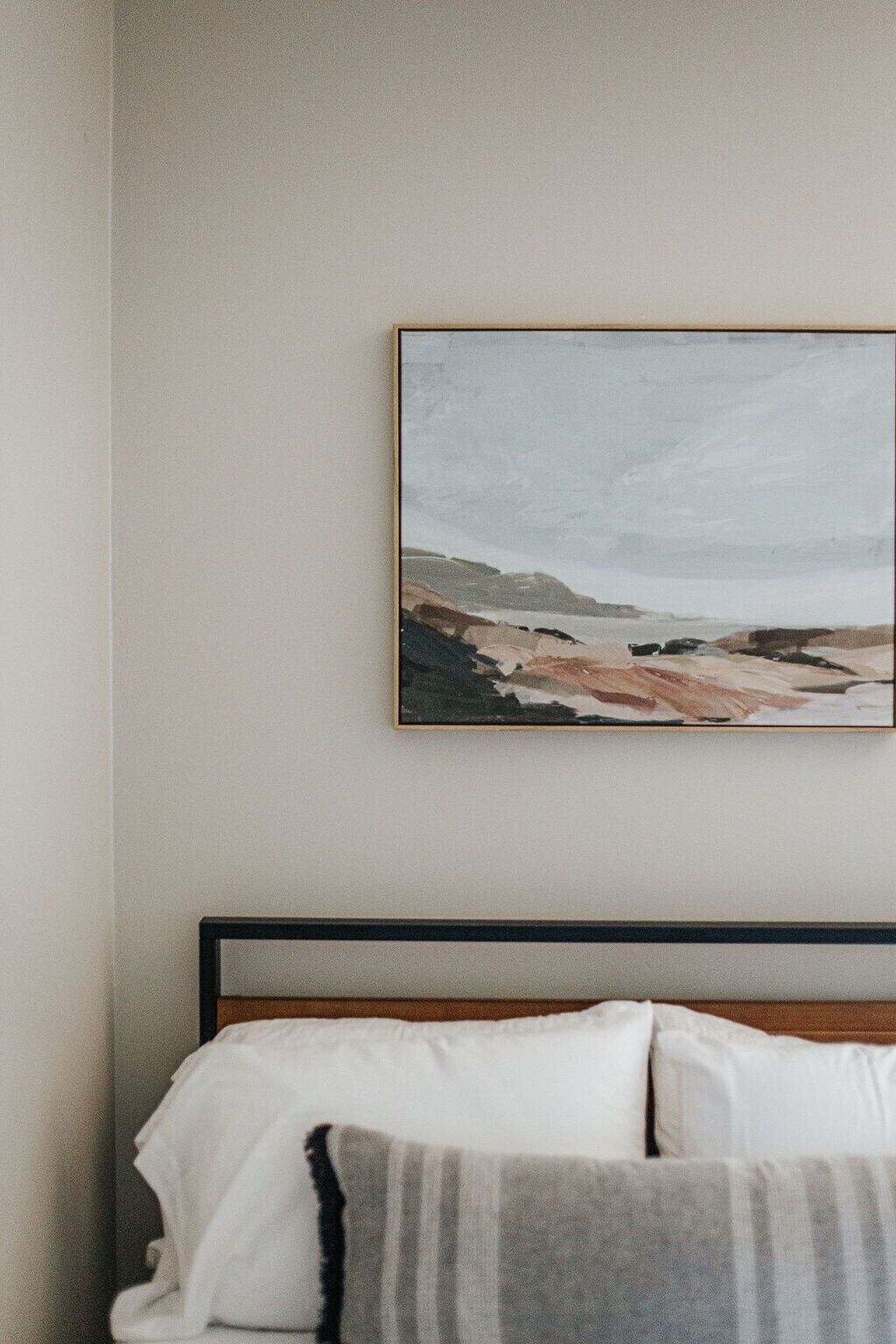 A bedroom with a bed, pillows, and a framed artwork on the wall.