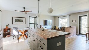 A modern kitchen with a wooden island, white chairs, and a dining table. - Hillside Haven (Faber)