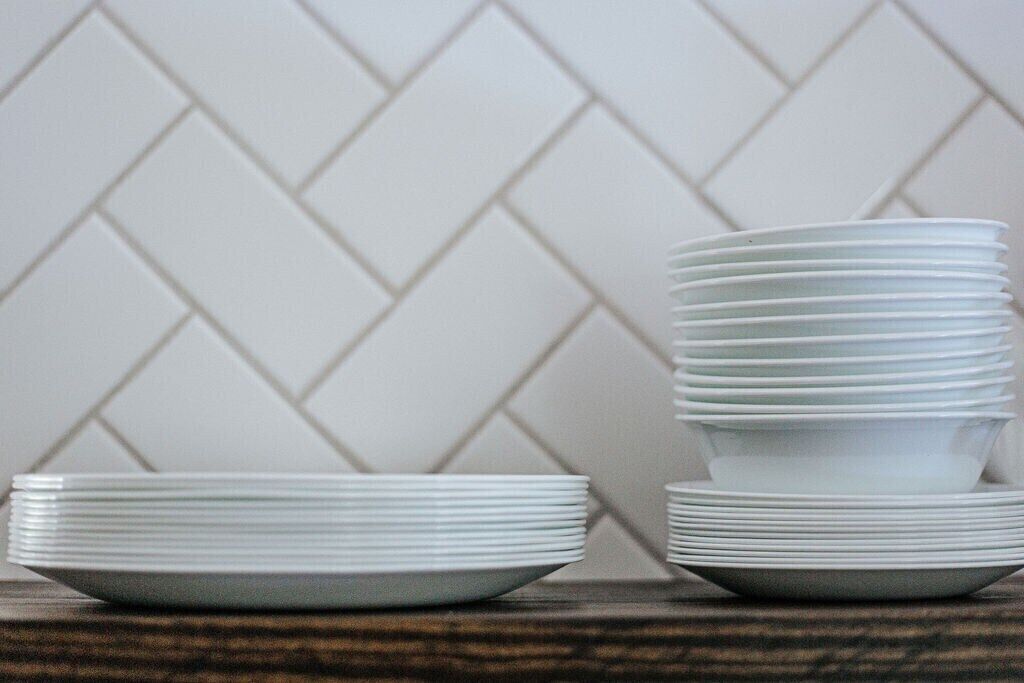 A stack of white plates on a wooden surface with a herringbone patterned tile backsplash.
