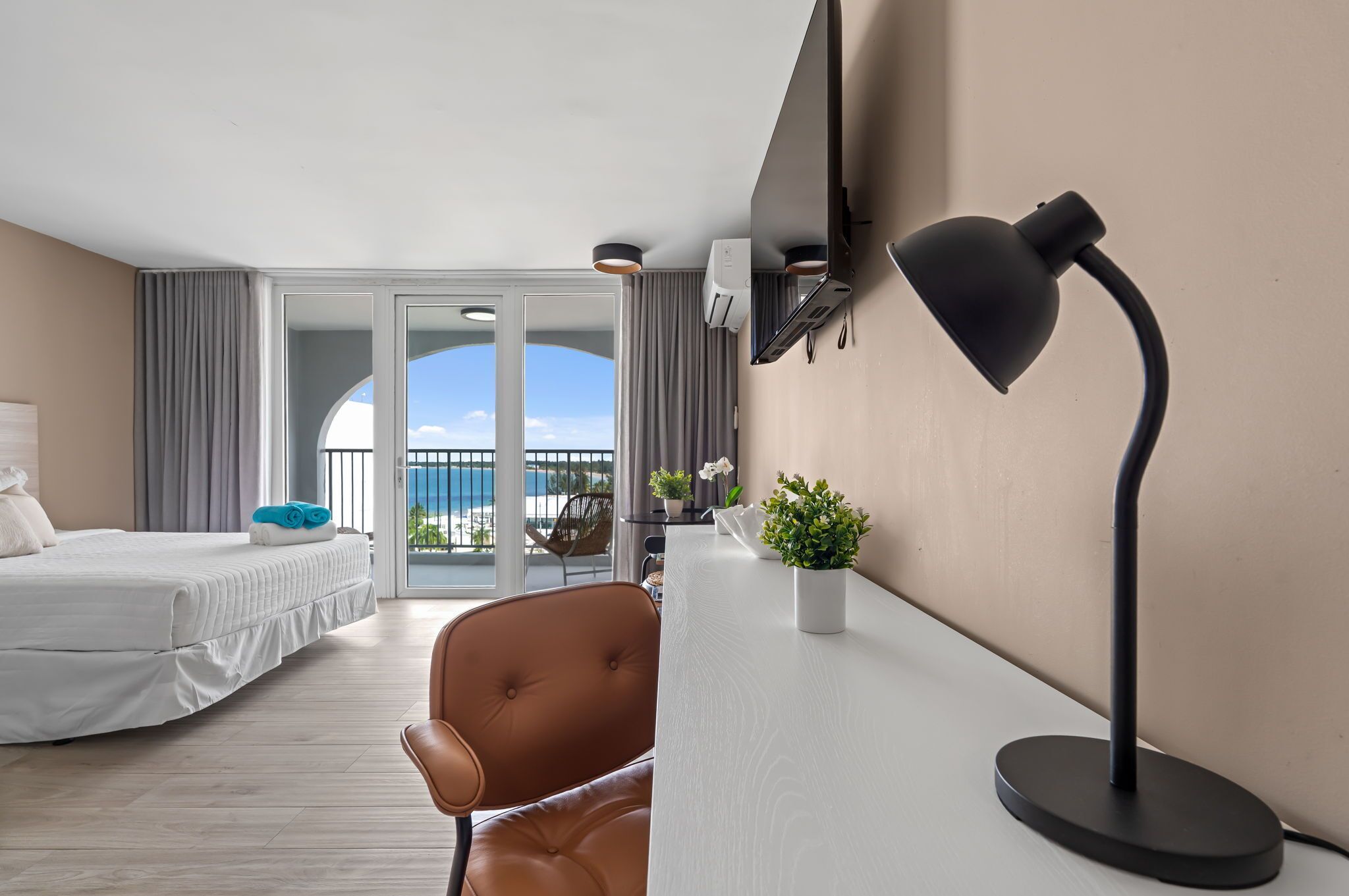 Een hotelkamer met een bed, een bureau, een stoel, een plant in pot en uitzicht op de omgeving.