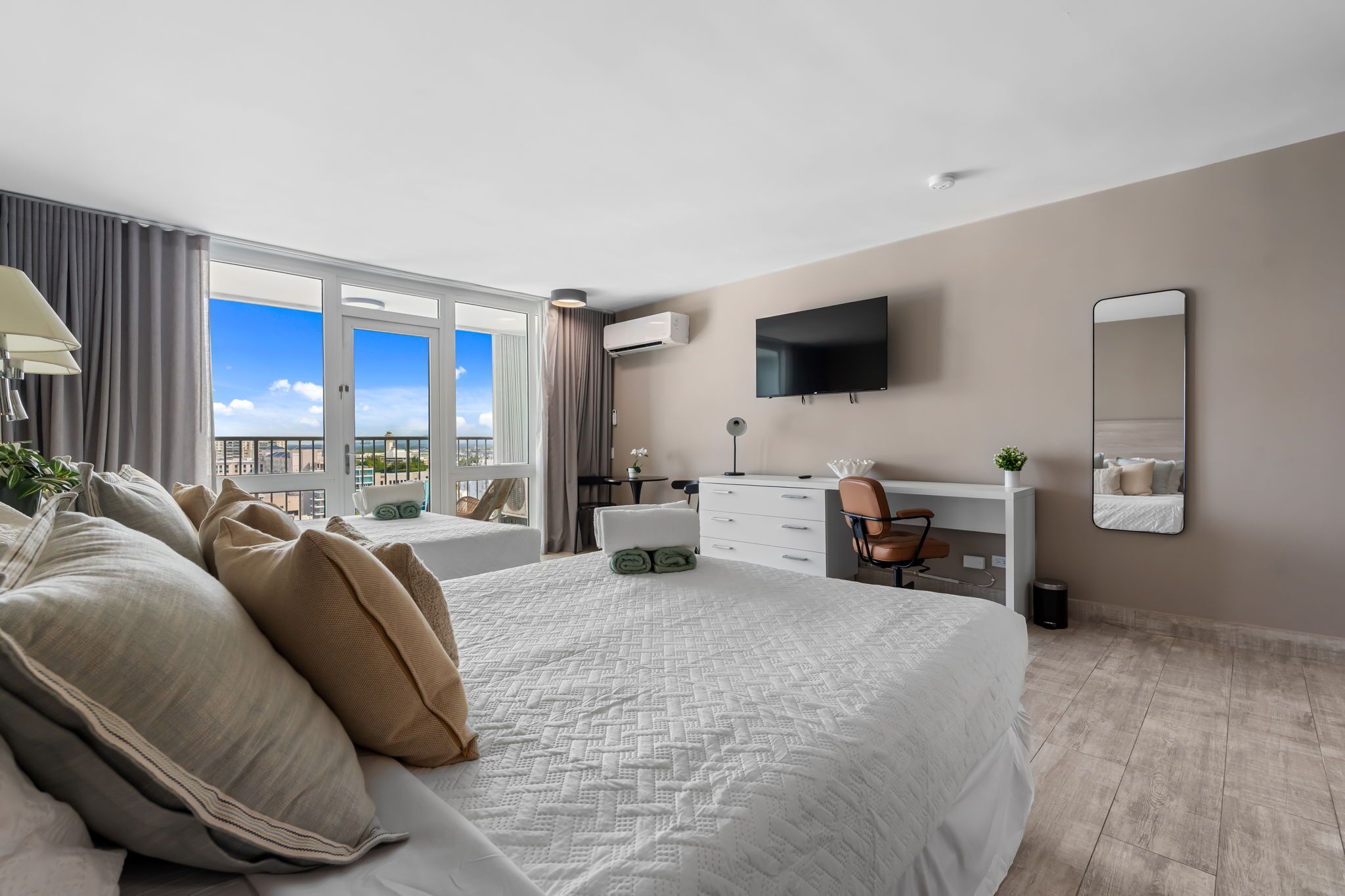 A hotel room with a large bed, a desk, a chair, a TV, and a view of the city.