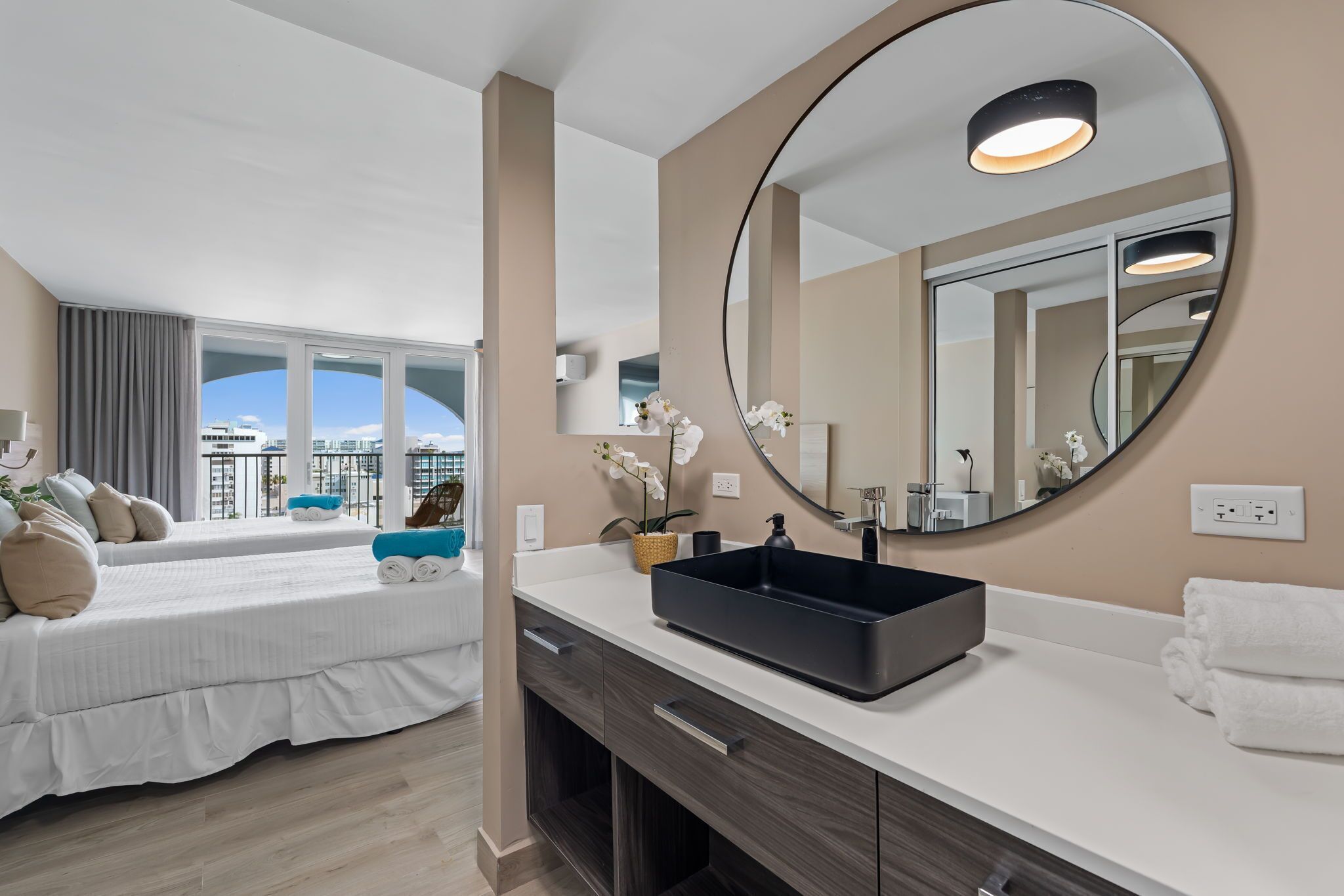 A hotel room with a large bed, a bathroom with a modern sink and mirror, and a view of the city.