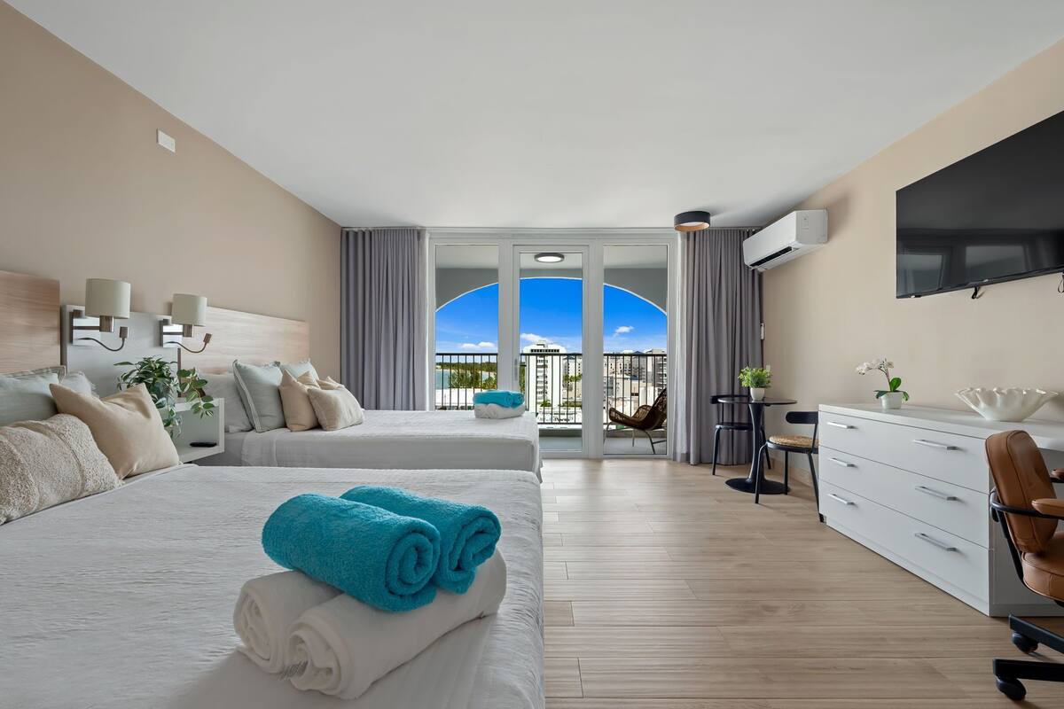 Habitación de hotel con dos camas, un escritorio, una silla, un televisor y un balcón con vistas.
