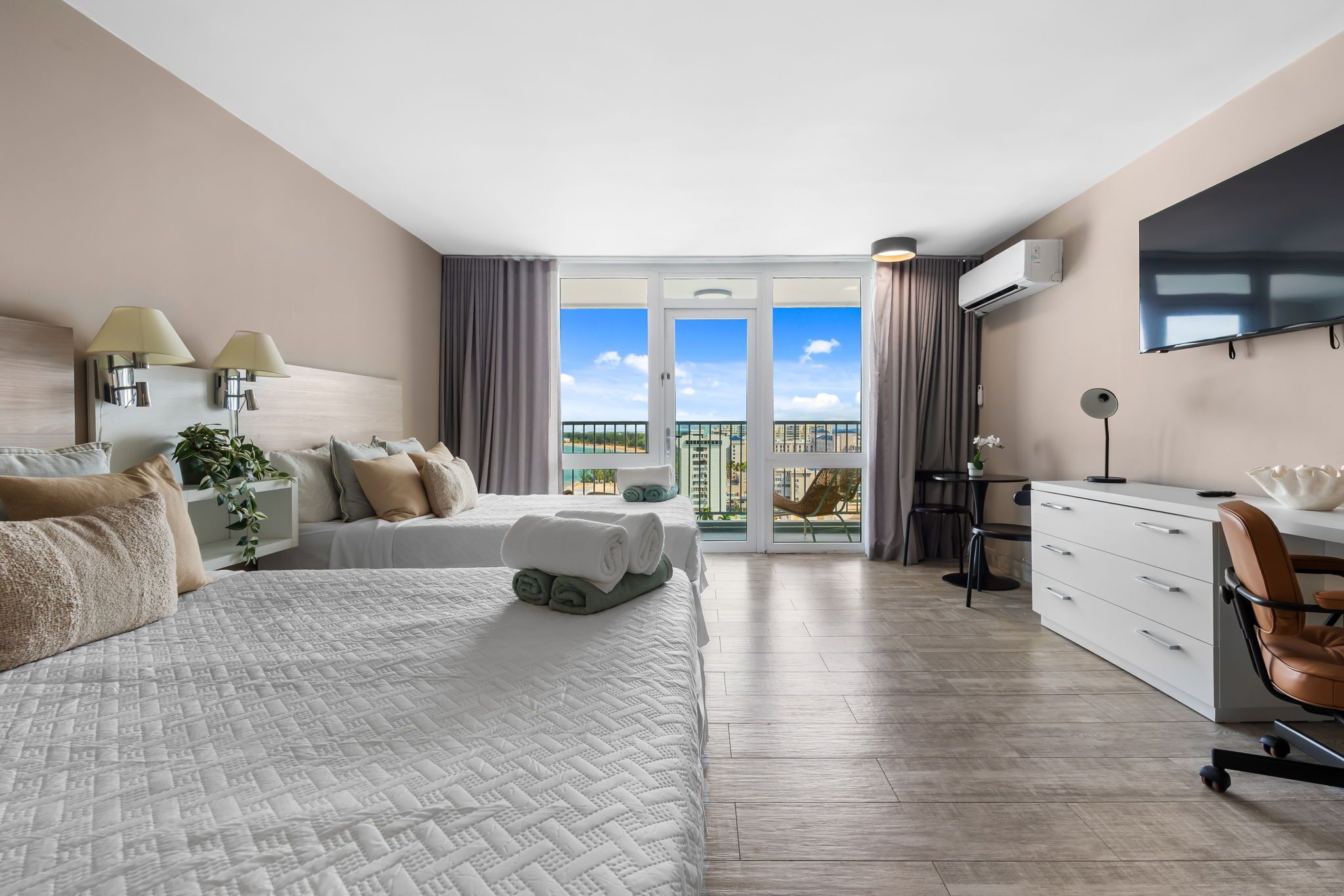 Habitación de hotel con cama, escritorio, silla, televisión y balcón con vistas.