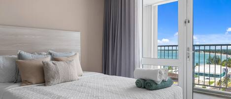 Habitación de hotel con una cama grande, vista a la playa y un balcón con barandilla.