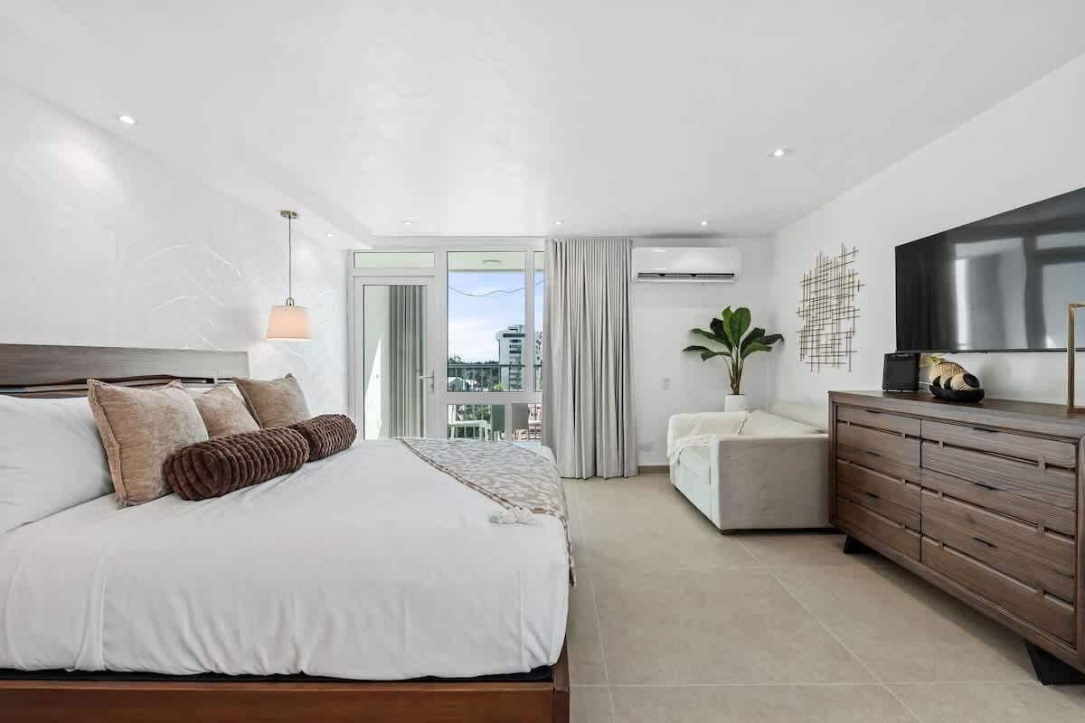 Un dormitorio moderno con una cama grande, un aparador, un televisor y vistas de la ciudad.