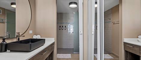 Un baño moderno con un espejo grande, dos lavamanos, una zona de ducha y una puerta de vidrio que da a una ducha a pie.