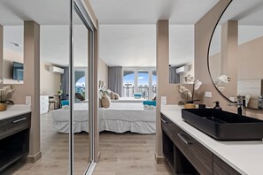 Habitación de hotel moderna con una cama grande, un lavabo negro, un espejo y vistas a la ciudad.