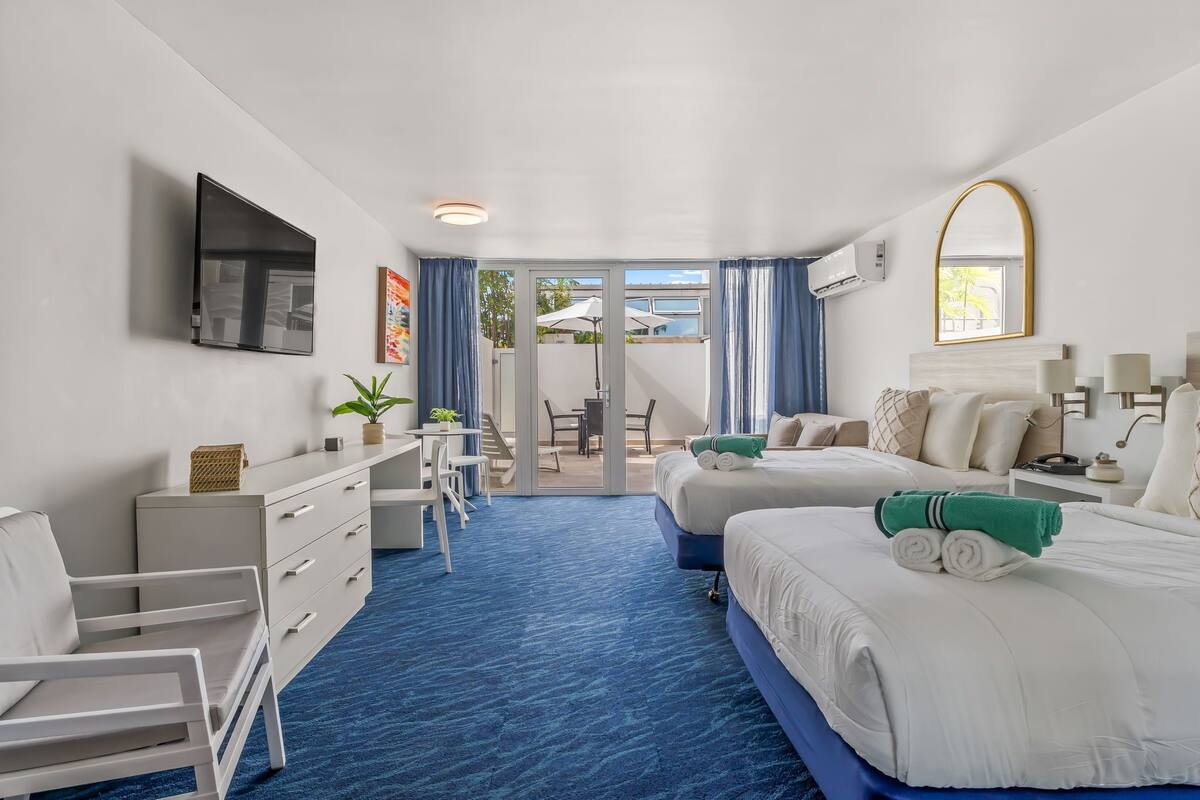 Habitación de hotel con televisión, escritorio, dos camas, balcón y vistas al exterior.