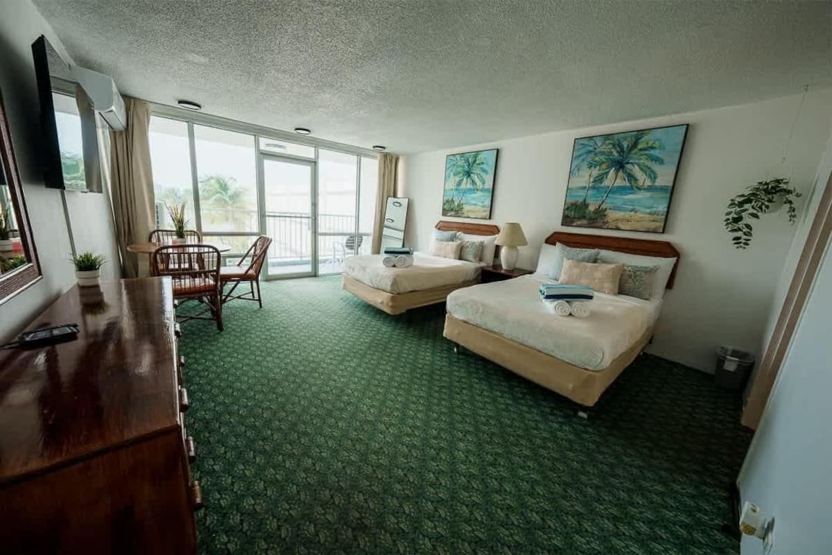 Habitación de hotel con dos camas, un balcón con vistas, un escritorio y una silla, y un televisor.