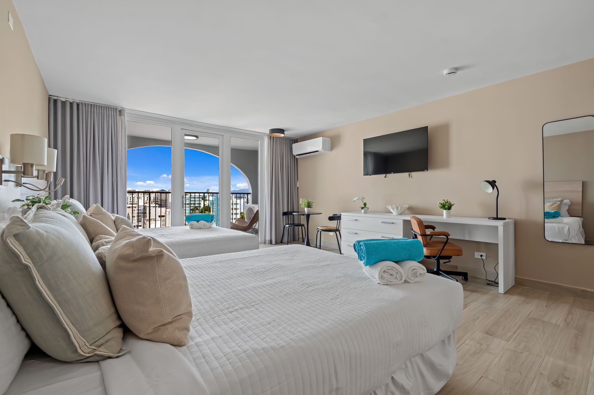 Ein Hotelzimmer mit zwei Betten, einem Schreibtisch, einem Stuhl, einem Fernseher und einem Balkon mit Blick.