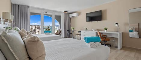 Ein Hotelzimmer mit zwei Betten, einem Schreibtisch, einem Stuhl, einem Fernseher und einem Balkon mit Blick.