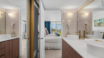 A modern hotel room with a large bed, two bathrooms, a view of the city, and a balcony.