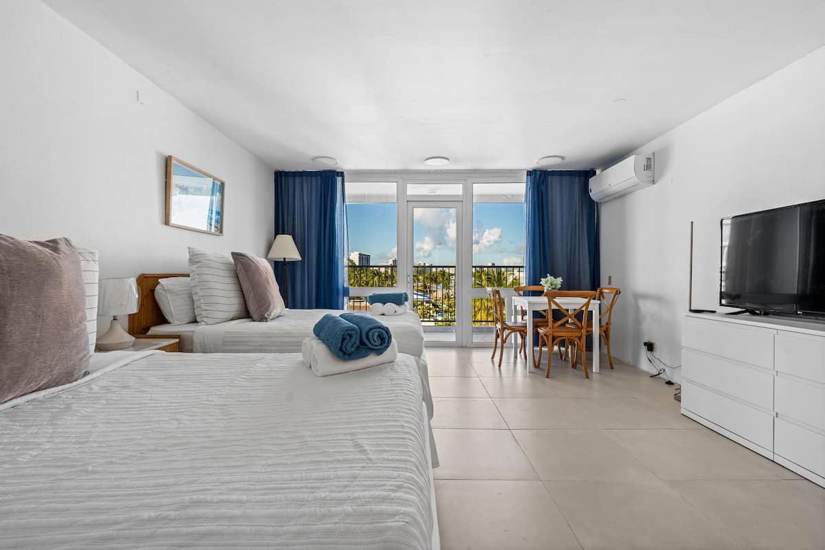 Una habitación de hotel con dos camas, un balcón, zona de comedor y televisor.
