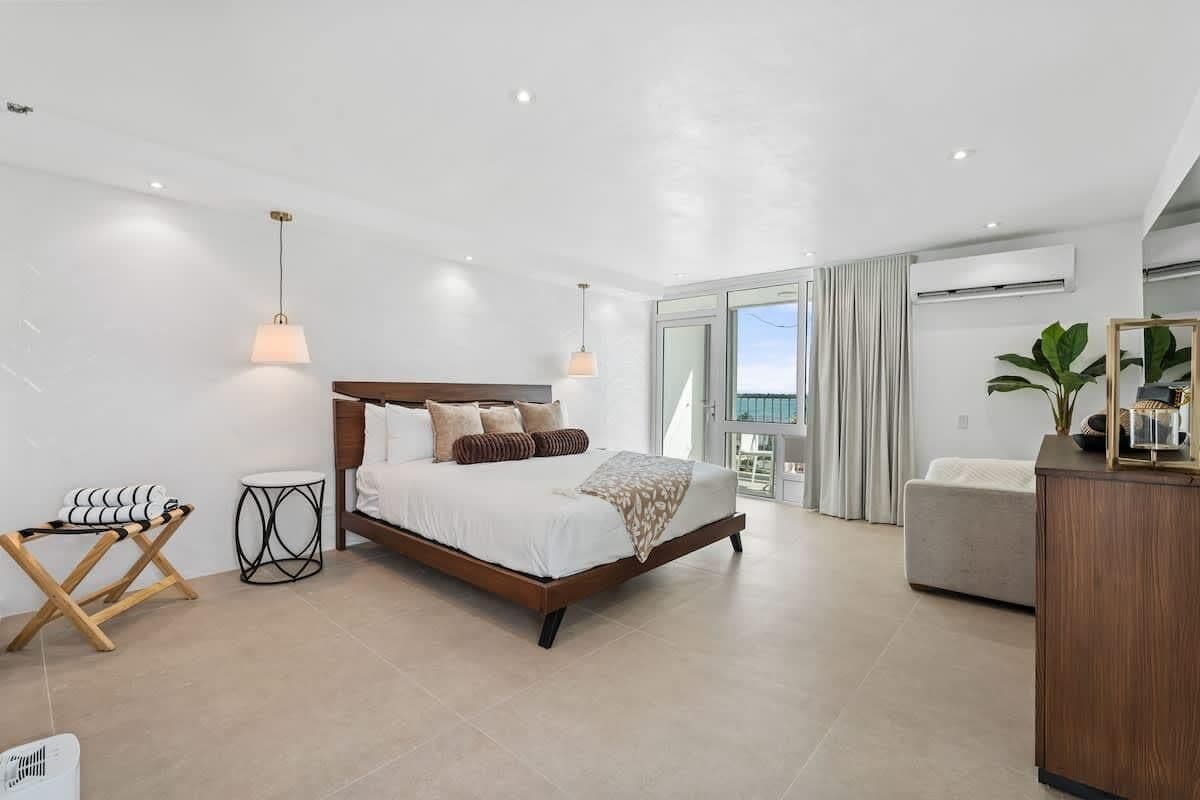 Un dormitorio moderno con una cama grande, mesitas de noche, una pequeña mesa redonda y vistas al exterior.