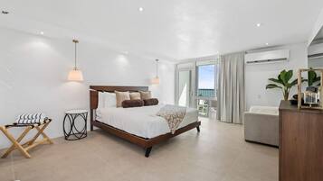 Un dormitorio moderno con una cama grande, mesitas de noche, una pequeña mesa redonda y vistas al exterior.