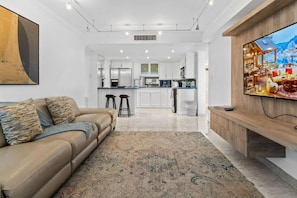 A modern living room with a sofa, a TV, and a kitchen in the background.