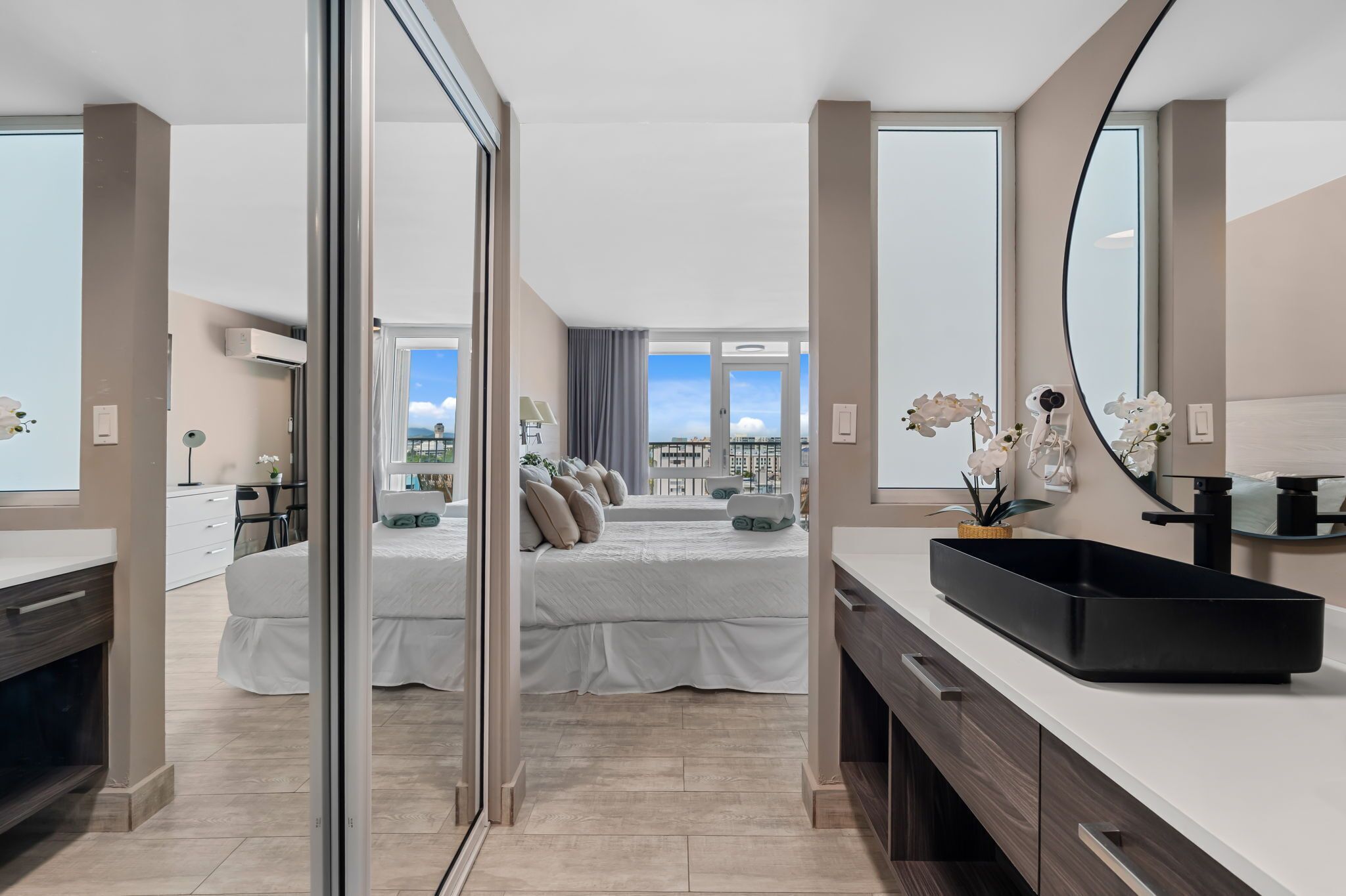 Une chambre d’hôtel moderne avec un grand lit, une salle de bain dotée d’un lavabo noir et une vue sur la ville.