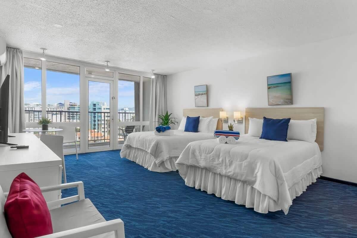 Habitación de hotel con dos camas, un escritorio, una silla y un balcón con vistas.
