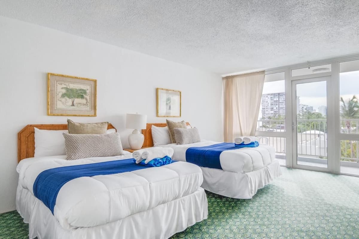 Habitación de hotel con dos camas, un ventanal con vistas y dos cuadros en la pared.