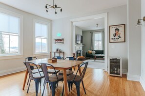 Un coin repas avec une table et des chaises en bois, un panneau lumineux au néon, un réfrigérateur et un téléviseur à l’arrière-plan.