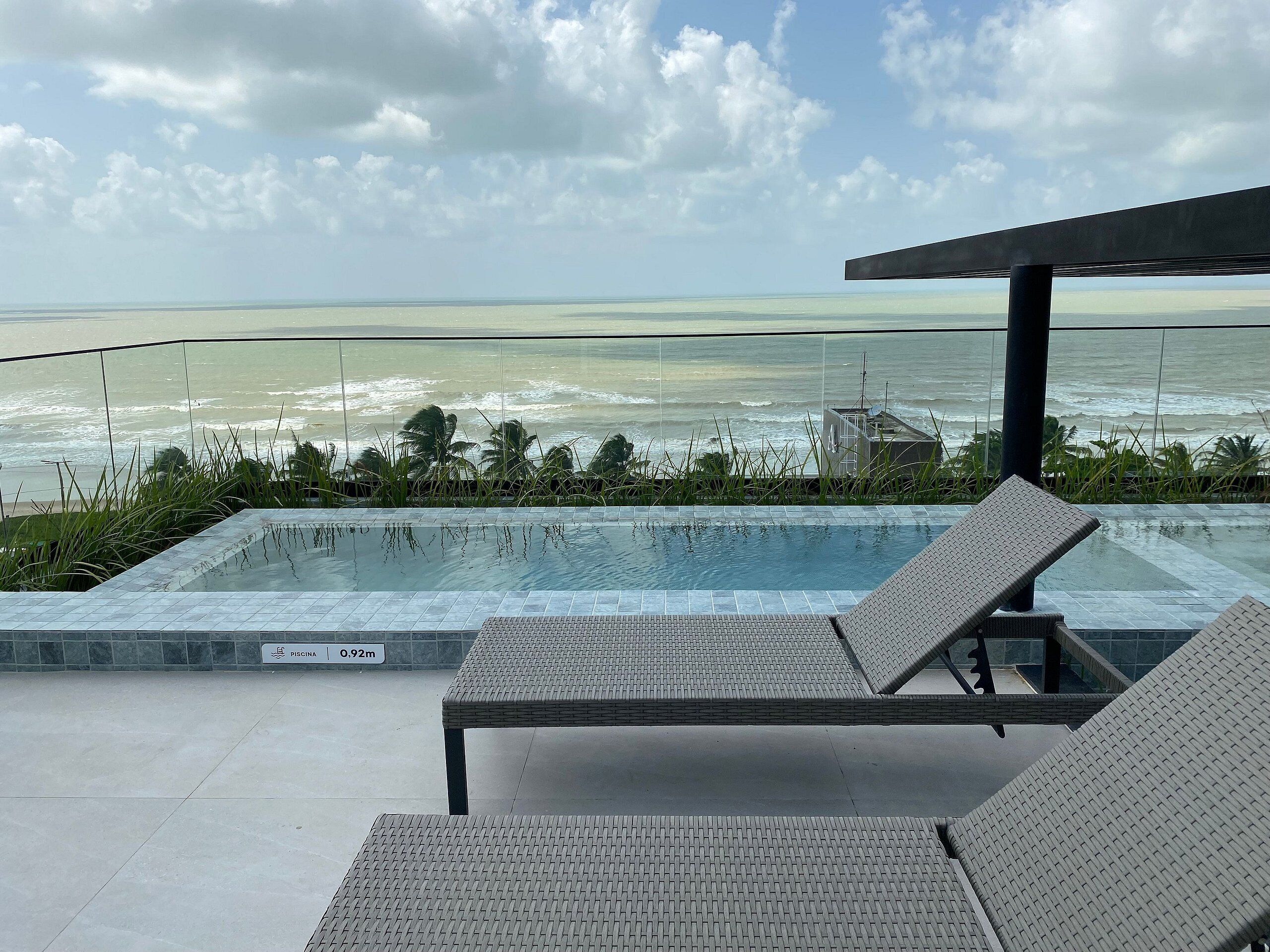 Une piscine avec deux chaises longues, un panneau indiquant une profondeur de 0,92 mètre et une vue sur l’océan.