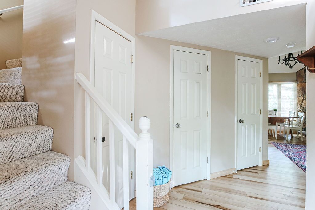 A staircase with white railings leading to a door, a hallway with wooden flooring, and a dining area in the background.