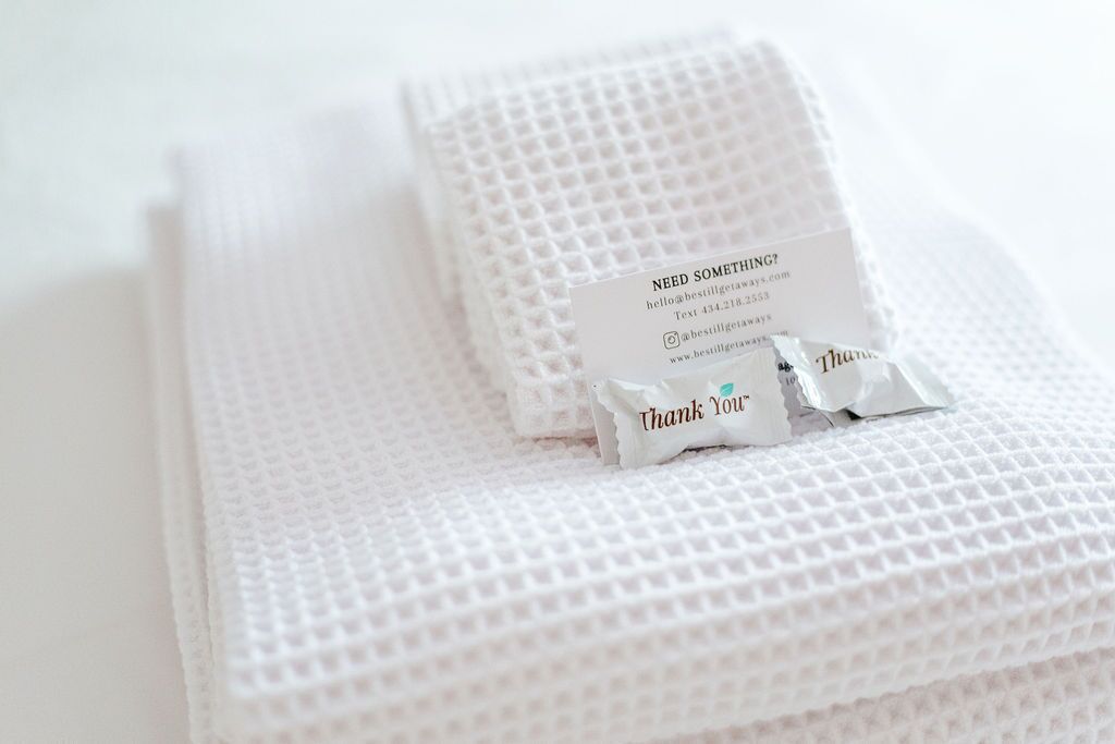 A neatly folded white towel with a thank you card and a small thank you note on a textured white surface.