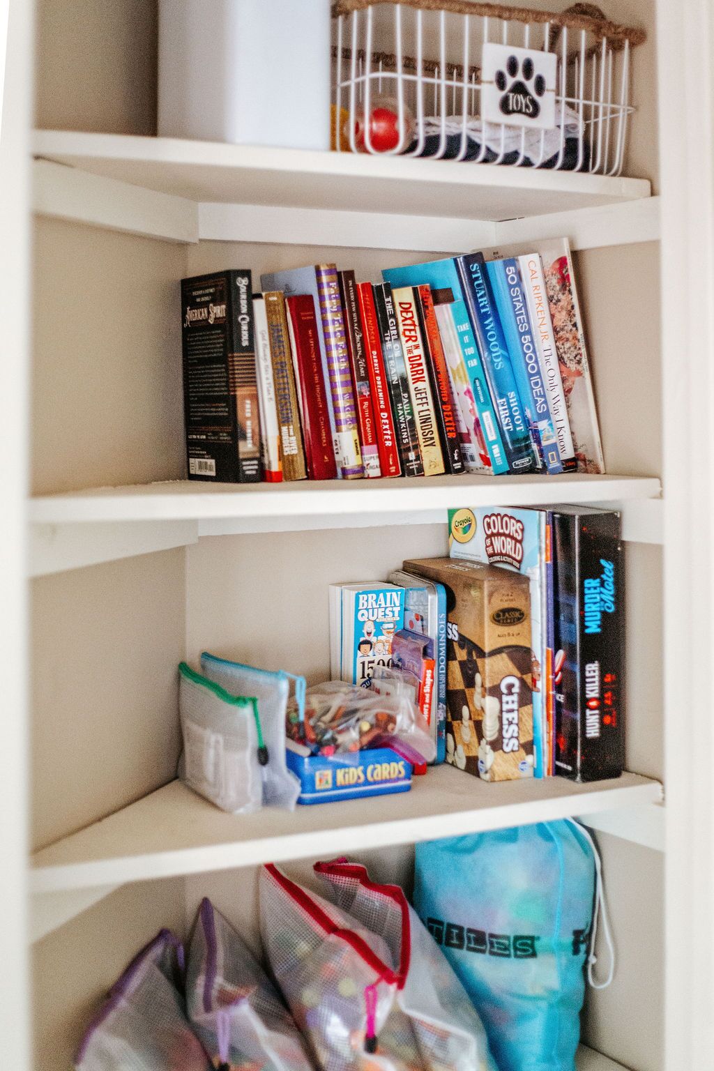 A bookshelf with various books, board games, and a toy cage.