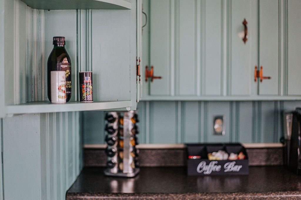 Een keuken met blauwgroene kastjes, een koffiebar en een fles olijfolie op het aanrecht.