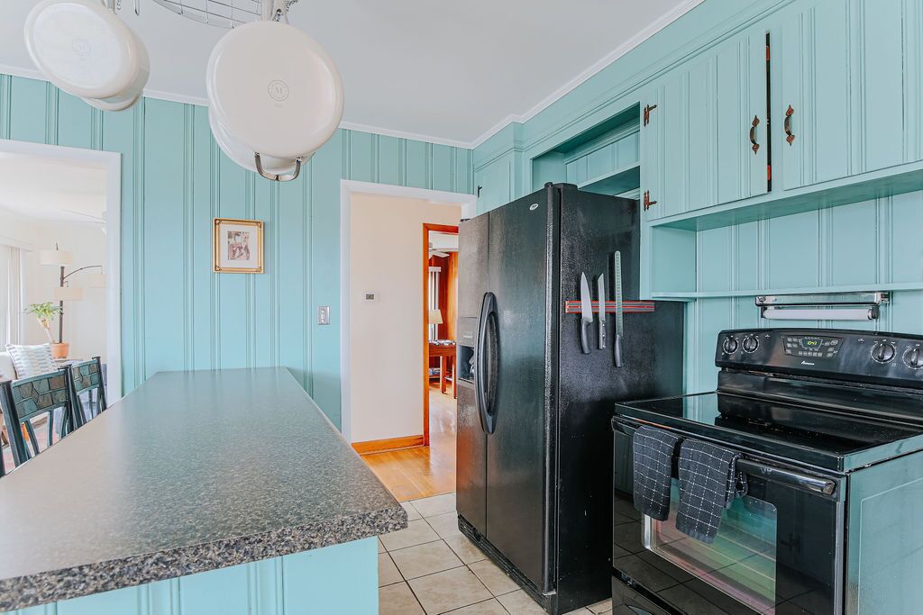A kitchen with teal cabinetry, a black refrigerator, and a stove.