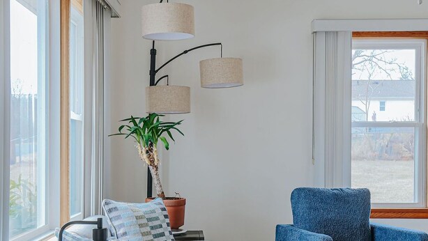 Ett vardagsrum med en soffa, en blå fåtölj, ett soffbord, en bordslampa, en golvlampa och en krukväxt.