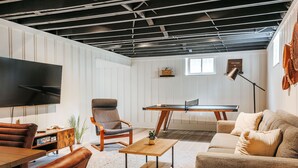 Una sala de estar con sofá, mesa de centro, televisor, mesa de juegos y una silla.