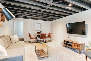 A modern living room with a dining area, a flat-screen TV, and a ceiling with exposed beams. - Lewis Mountain Retreat (Charlottesville)