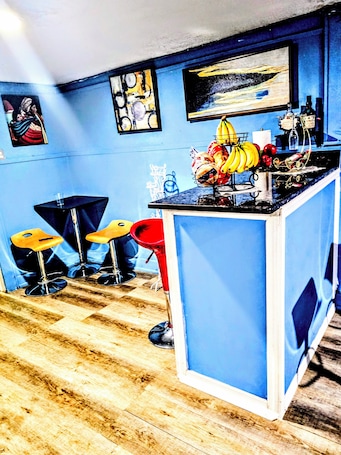A bar area with stools, a counter with bottles, and artwork on the walls.. 20 min from airport 2-bedroom apartment with AC in vibral Newark