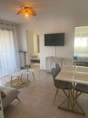Ein modernes Wohnzimmer mit Flachbildfernseher, Essbereich mit Tisch und Stühlen, einer Couch und einer dekorativen Leuchte.