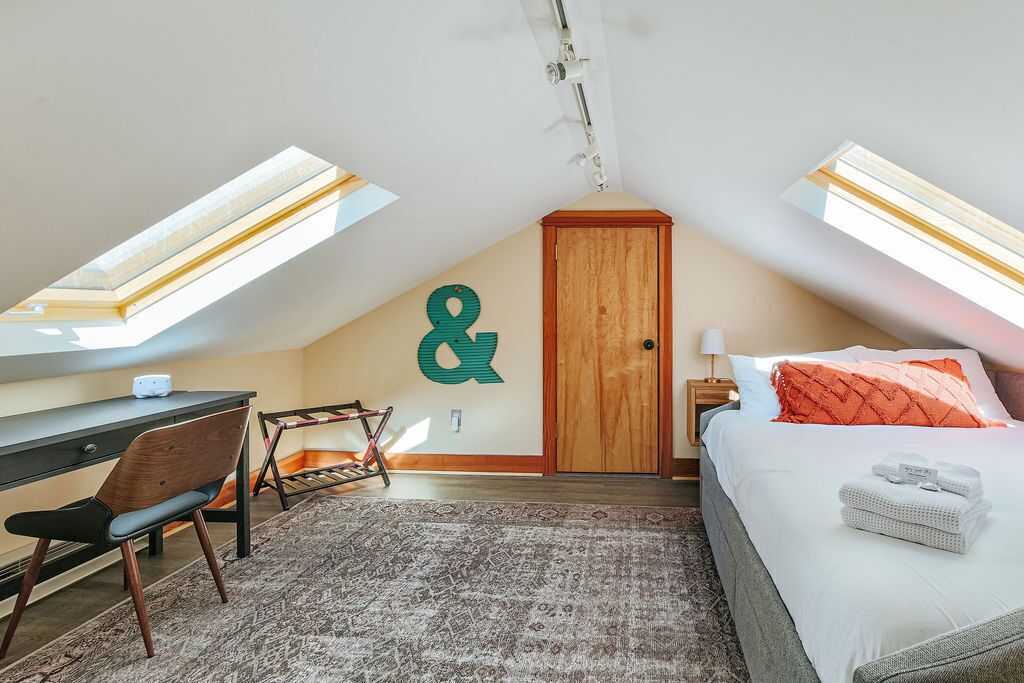 A bedroom with a desk, a bed, a chair, and a large window.