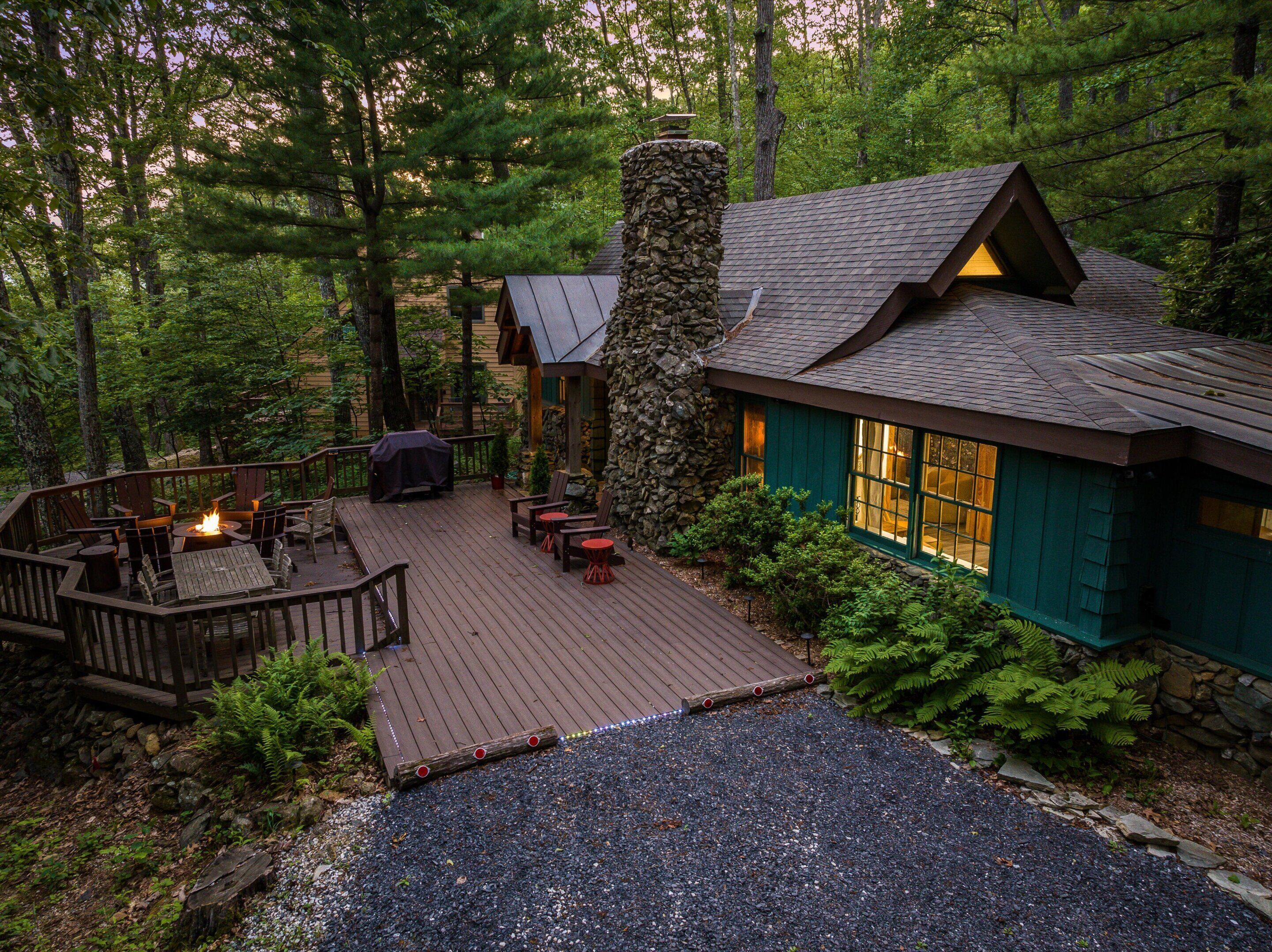 A cabin with a deck, outdoor seating, and a stone chimney.