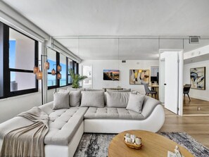 Ein modernes Wohnzimmer mit einer Eckcouch, einem Couchtisch und Blick auf die Stadt durch große Fenster.