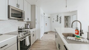 A modern kitchen with white cabinetry, a stainless steel oven, a microwave, and a large island with a sink. - Mountain View Vista (Nellysford)