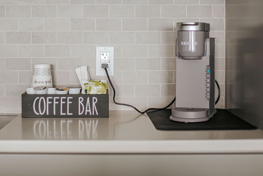 A coffee maker on a countertop with a coffee bar sign, a coffee cup, and a coffee pod.