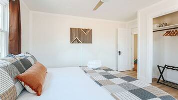 A bedroom with a bed, a ceiling fan, a geometric wall decoration, a folded towel on the floor, and a closet with hanging clothes.