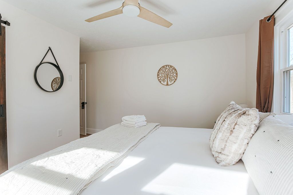A bedroom with a bed, a ceiling fan, a wall-mounted circular decoration, and a window with curtains.