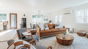 Uma sala de estar espaçosa com um sofá de couro marrom, uma mesa de centro de madeira e um espaço de jantar com mesa e cadeiras.