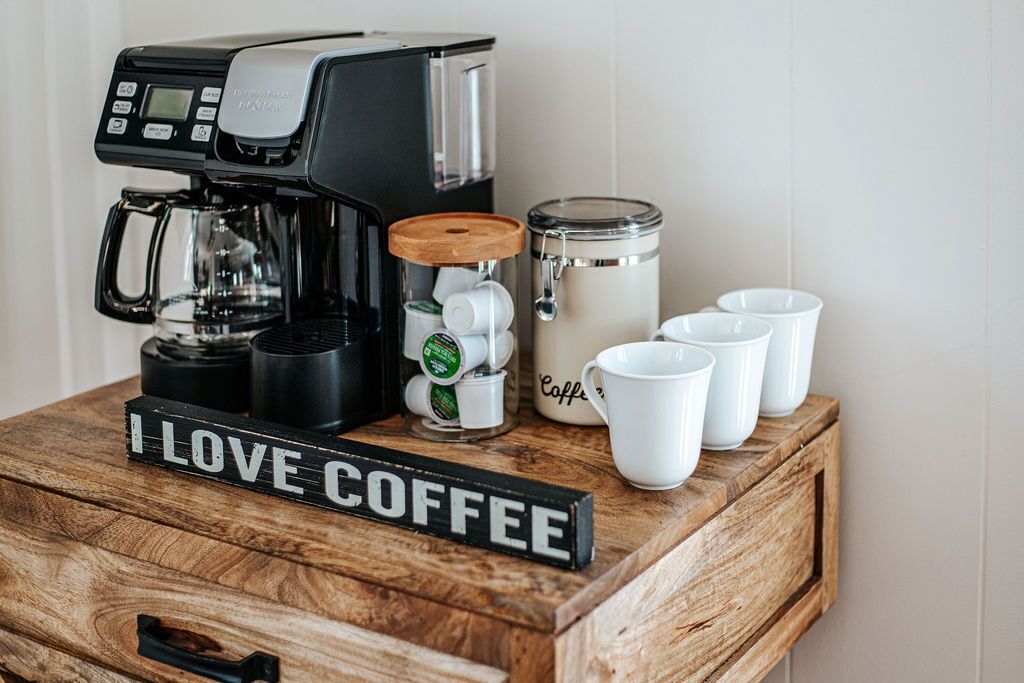 A coffee maker, a coffee grinder, a coffee storage container, and four white coffee cups on a wooden table.