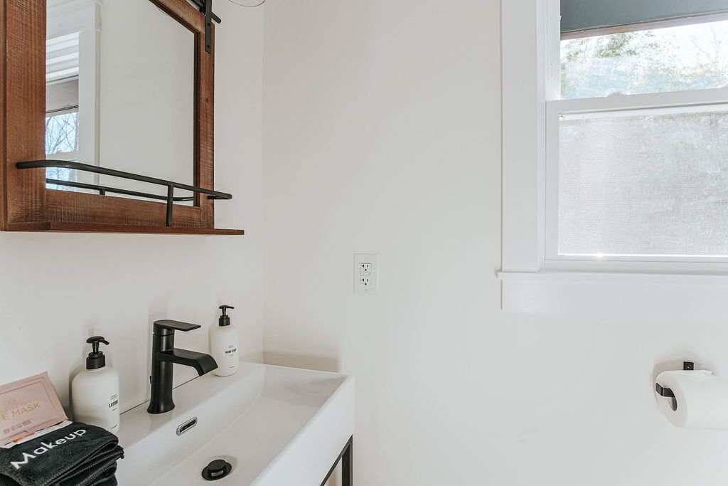 Une salle de bain avec un lavabo blanc, un robinet noir et un miroir doté d’un cadre en bois.