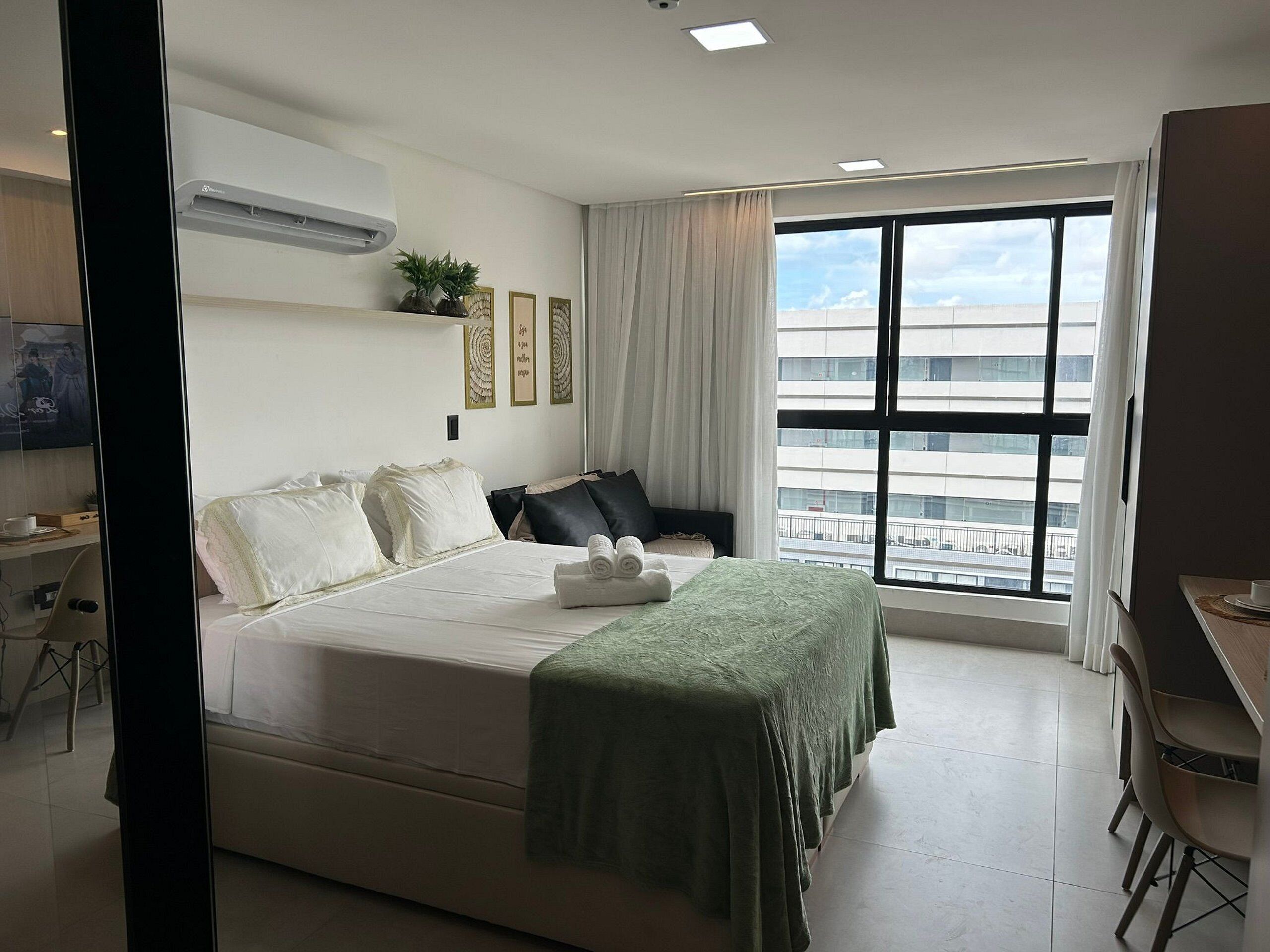 Ein Hotelzimmer mit Bett, Schreibtisch, Stuhl, einem Fenster mit Blick auf Gebäude und einer Klimaanlage.