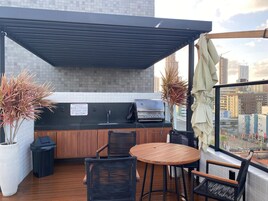 Cocina exterior con parrilla, lavadero y zona de comedor con sillas y mesa.