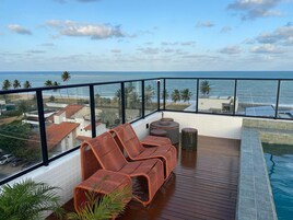 Un balcon avec des fauteuils en osier, une petite table et une vue sur l’océan et la plage.